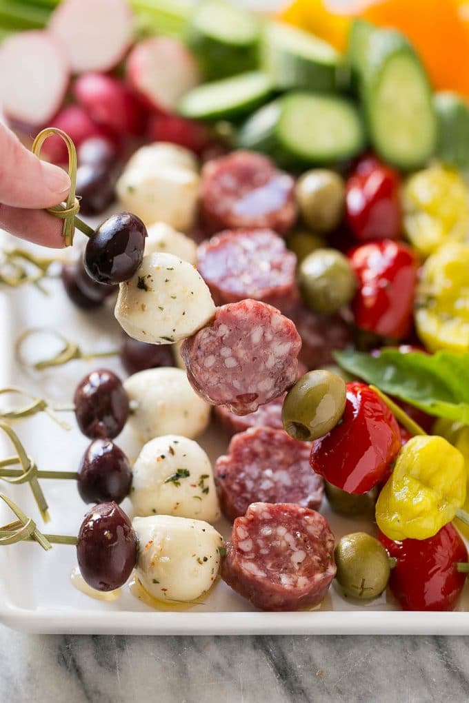 Antipasto Skewers Recipe | Easy Antipasto | Best Antipasto #antipasto #skewers #appetizer #uzhal A hand holding up a skewer of salami, cheese and olives.