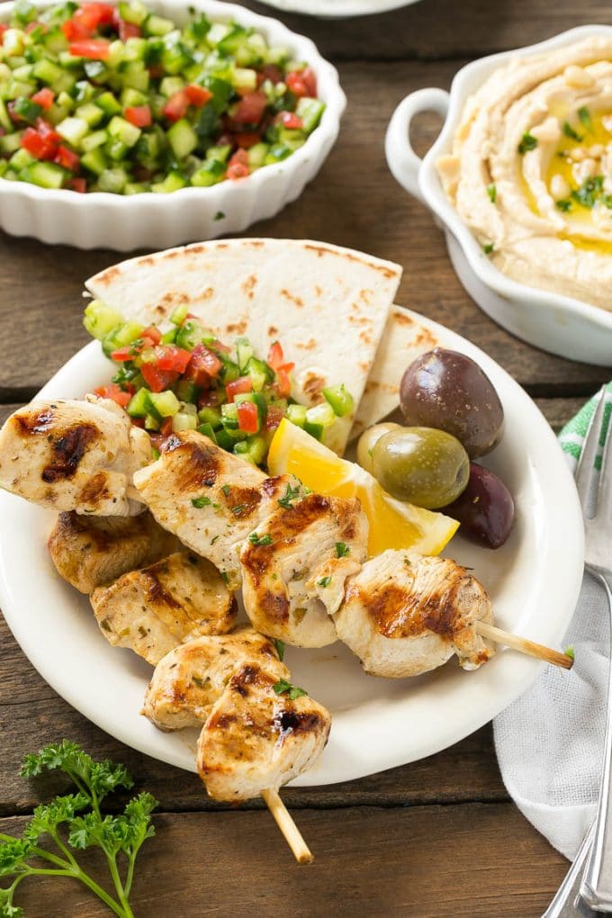 A plate of skewers with olives and pita bread.