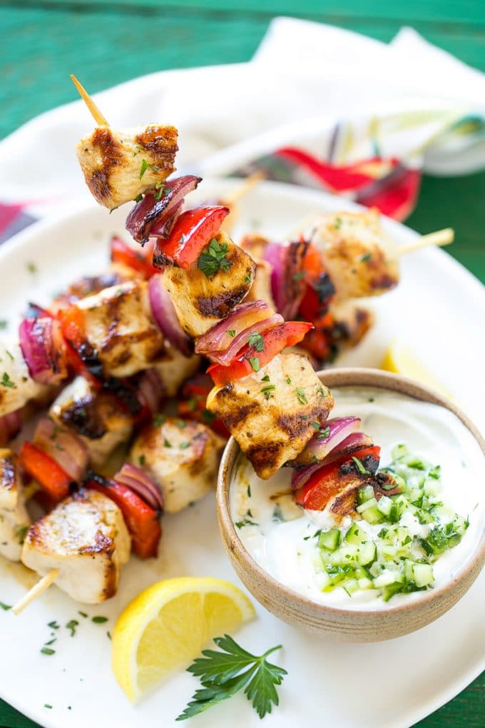 Skewered meat and veggies being dipped onto cucumber yogurt sauce.