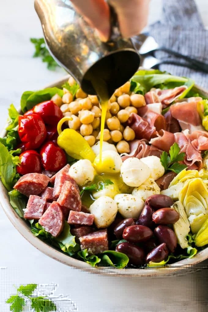 Antipasto Salad Recipe | Italian Salad | Main Course Salad | Antipasto Recipe #salad #salami #italianfood #dinner #lunch #uzhal A pitcher of dressing being poured over antipasto salad.