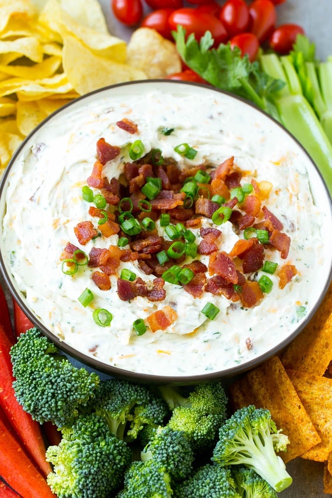 Bacon Ranch Dip Recipe | Homemade Ranch Dip | Easy Dip Recipe | Cheddar Ranch Dip #ranch #ranchdip #bacondip #dip #snack #uzhal #baconranchdip A bowl of creamy bacon cheddar ranch dip surrounded by vegetables and chips.