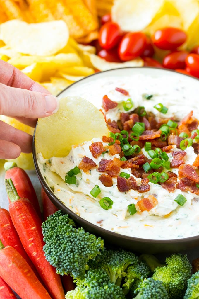 Bacon Ranch Dip Recipe | Homemade Ranch Dip | Easy Dip Recipe | Cheddar Ranch Dip #ranch #ranchdip #bacondip #dip #snack #uzhal #baconranchdip A hand scooping up bacon ranch dip with a potato chip.