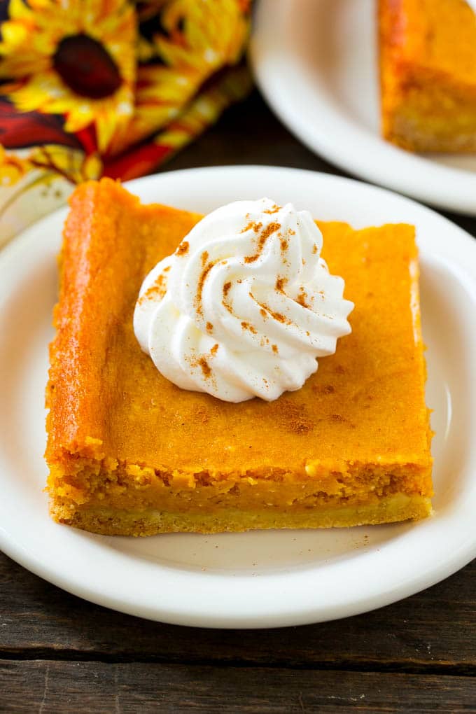 Pumpkin Gooey Butter Cake Recipe | Pumpkin Cake Recipe | Gooey Butter Cake | Pumpkin Dessert | Thanksgiving Dessert #pumpkin #cake #pumpkincake #gooeybuttercake #dessert #uzhal A slice of pumpkin gooey butter cake topped with whipped cream.