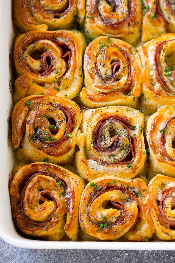 Ham and Cheese Pinwheels Recipe | Ham and Cheese Roll Ups | Ham and Cheese Rolls | Ham and Cheese Bread Rolls #ham #cheese #appetizer #pinwheels #uzhal Ham and cheese pinwheels in a baking dish topped with parsley.