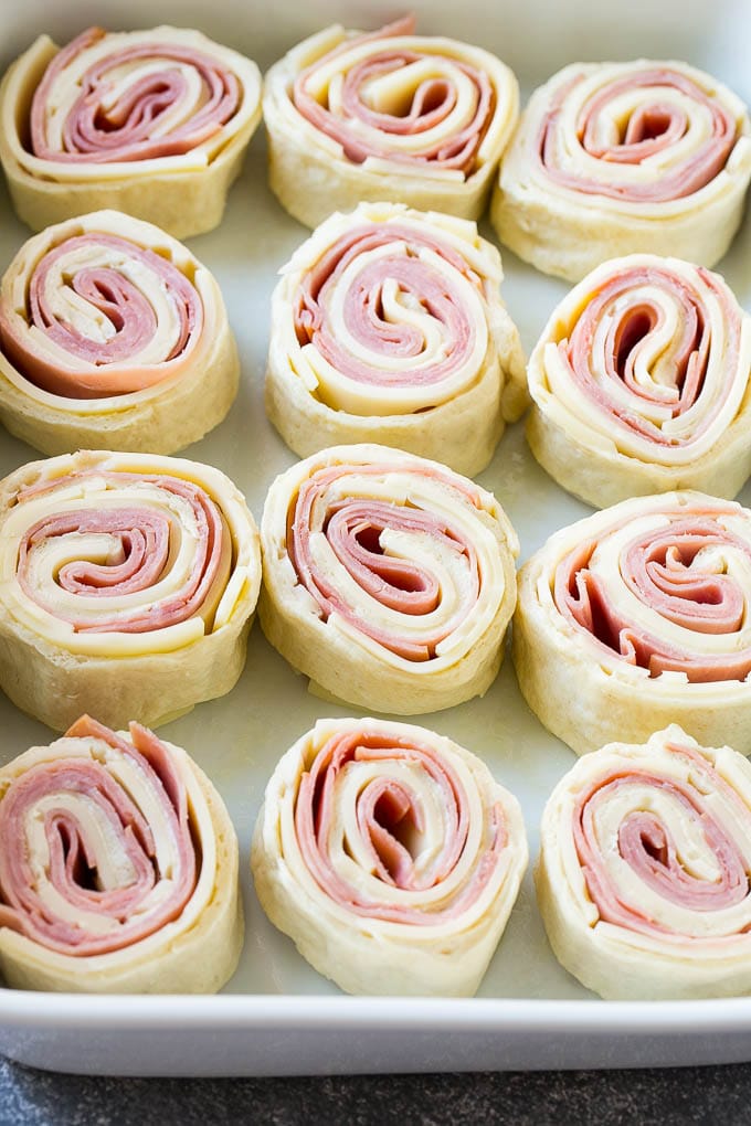 Ham and Cheese Pinwheels Recipe | Ham and Cheese Roll Ups | Ham and Cheese Rolls | Ham and Cheese Bread Rolls #ham #cheese #appetizer #pinwheels #uzhal Rolled up ham, cheese and pizza dough circles in a baking dish.