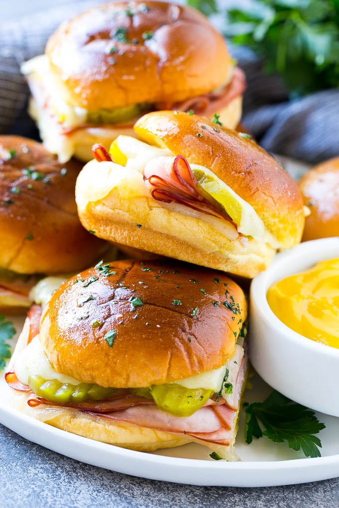 Cuban Sliders Recipe | Cuban Sandwich Recipe | Slider Sandwiches | Ham and Cheese Sliders #sliders #sandwiches #ham #cheese #appetizer #uzhal A plate full of Cuban sliders with cheese, pickles and ham on buns.