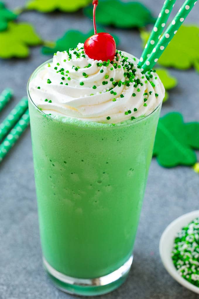 Shamrock Shake Recipe | McDonald's Shamrock Shake | Saint Patrick's Day Drink | Mint Milkshake #milkshake #stpatricksday #saintpatricksday #mint #uzhal A glass of shamrock shake topped with whipped cream, sprinkles and a cherry.