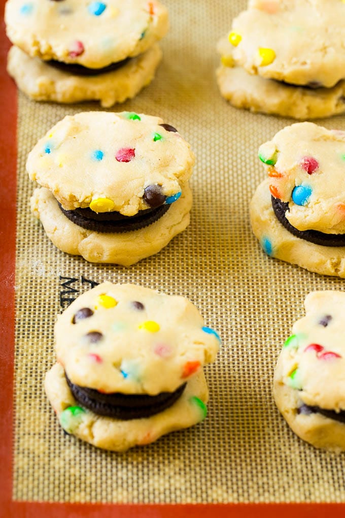 Oreo Stuffed Cookies Recipe | M&M's cookies | Stuffed Cookies #cookies #chocolate #oreos #dessert #baking #uzhal Cookie dough sandwiched around Oreos on a baking sheet.
