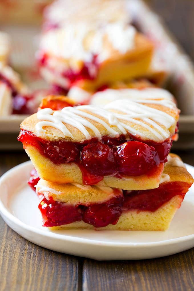 Cherry Bars Recipe | Cherry Pie Bars | Cherry Cookies | Bar Cookies #cookies #bars #cherry #baking #dessert #sweets #uzhal Two cherry bars on a plate with a pan of bars in the background.