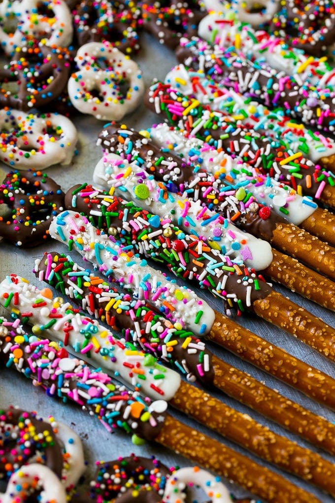 Chocolate Covered Pretzels Recipe | Sprinkle Pretzels | No Bake Dessert #pretzels #chocolate #christmas #sprinkles #candy #uzhal A sheet pan with coated twists and rods decorated with rainbow sprinkles.