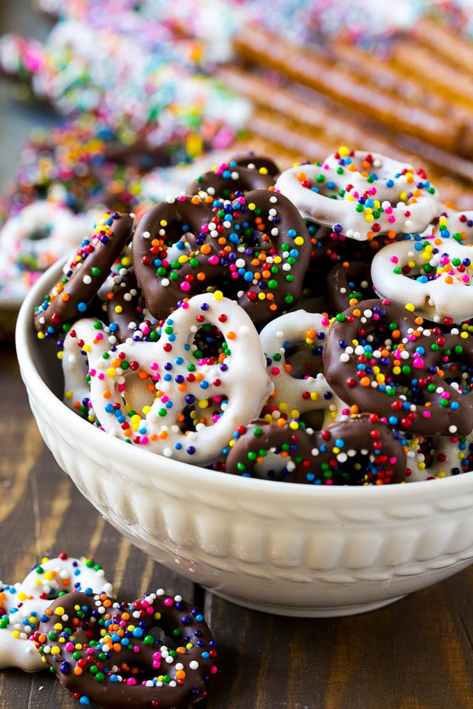 Chocolate Covered Pretzels Recipe | Sprinkle Pretzels | No Bake Dessert #pretzels #chocolate #christmas #sprinkles #candy #uzhal A bowl of chocolate covered pretzels decorated with rainbow sprinkles.