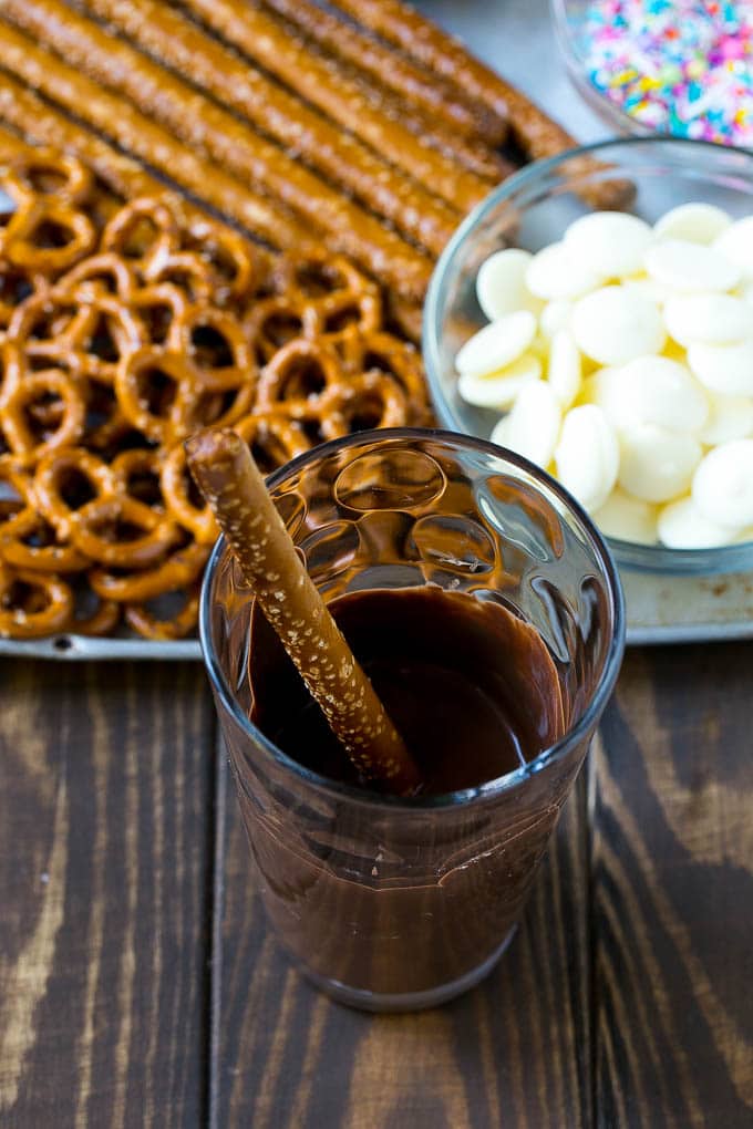 Chocolate Covered Pretzels Recipe | Sprinkle Pretzels | No Bake Dessert #pretzels #chocolate #christmas #sprinkles #candy #uzhal A rod in a glass full of melted chocolate.