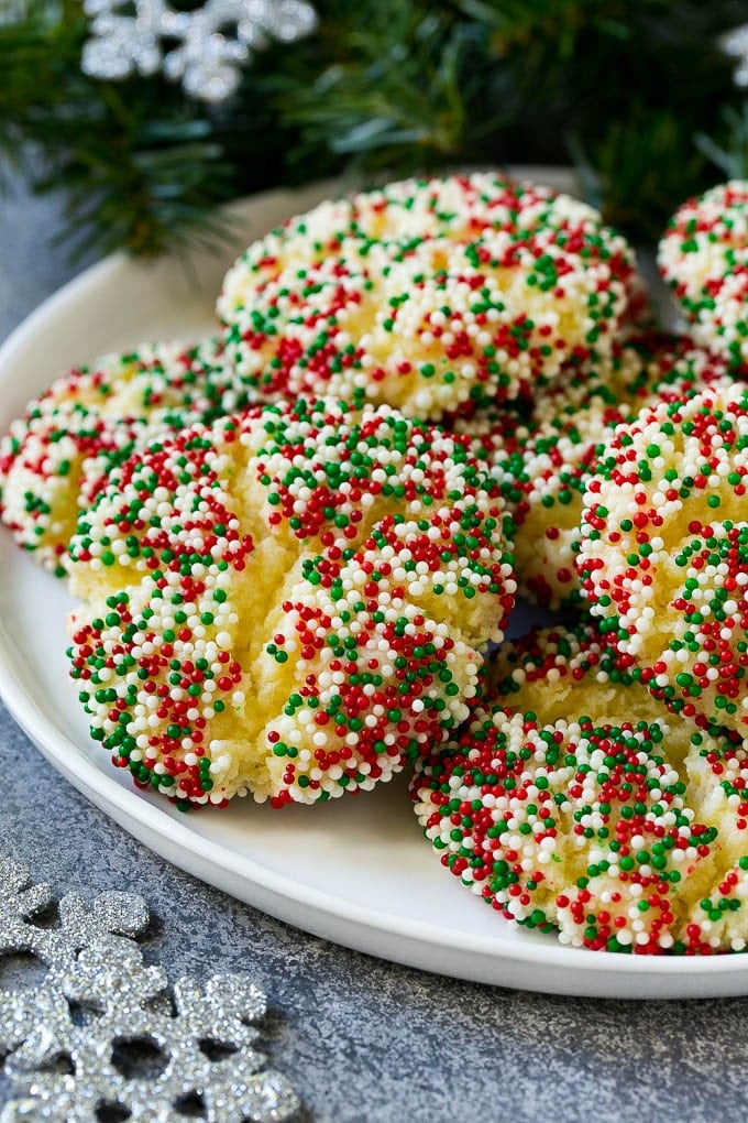 Gooey Butter Cookies Recipe | Cake Mix Cookies | Sprinkle Cookies | Christmas Cookies #cookies #butter #sprinkles #christmas #dessert #baking #uzhal A plate of gooey butter cookies covered in holiday sprinkles.
