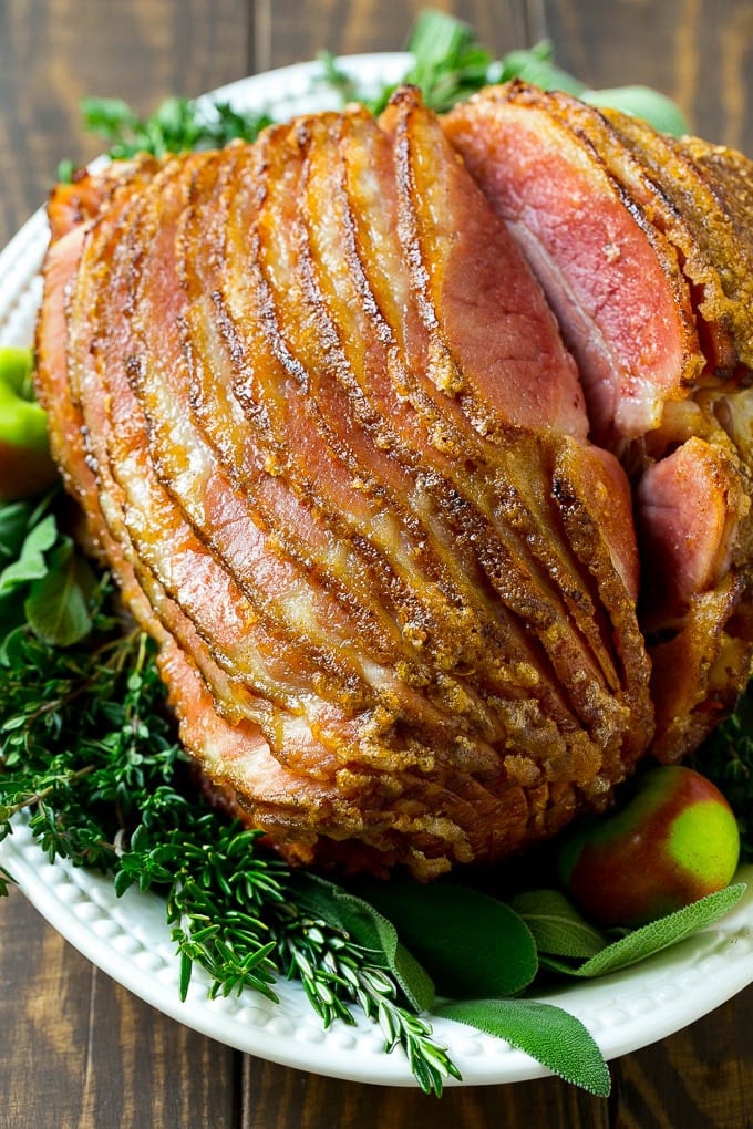 Honey Baked Ham Recipe | Glazed Ham | Holiday Ham #ham #dinner #uzhal #christmas #thanksgiving #easter A spiral cut honey baked ham on a serving platter garnished with fresh herbs.