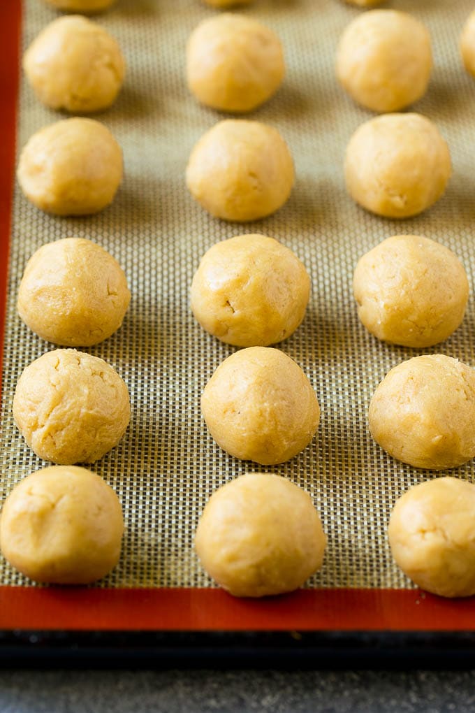 Peanut Butter Blossoms Recipe | Hershey Kiss Cookies | Chocolate Peanut Butter Cookies #cookies #peanutbutter #chocolate #dessert #baking #christmas #christmascookies #uzhal Balls of dough on a baking sheet.