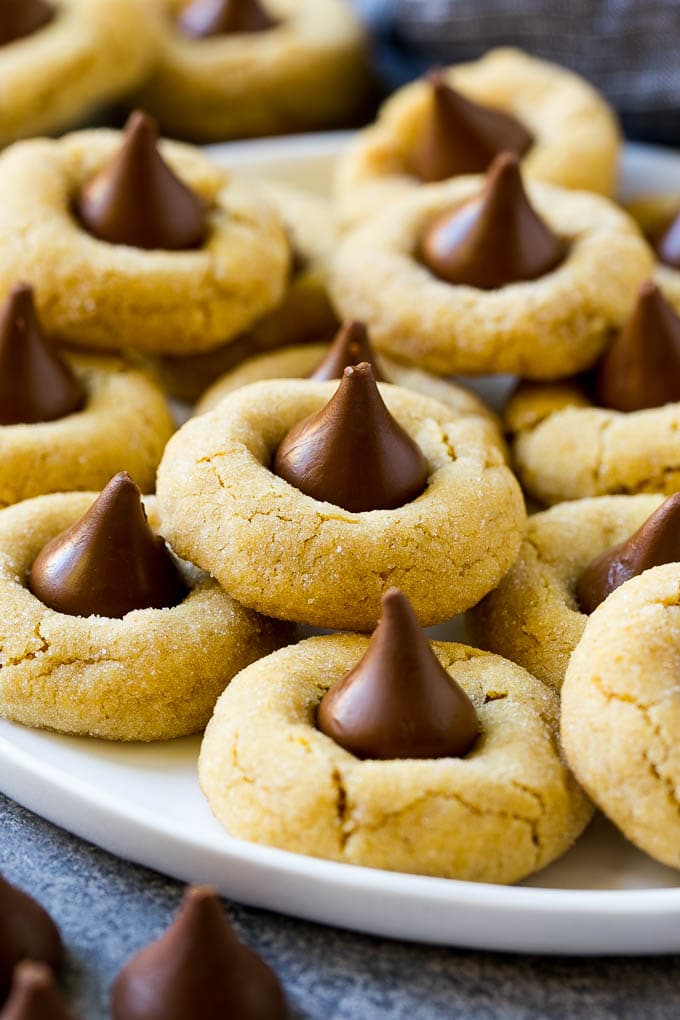 Peanut Butter Blossoms Recipe | Hershey Kiss Cookies | Chocolate Peanut Butter Cookies #cookies #peanutbutter #chocolate #dessert #baking #christmas #christmascookies #uzhal A plate with peanut butter blossoms stacked onto it.