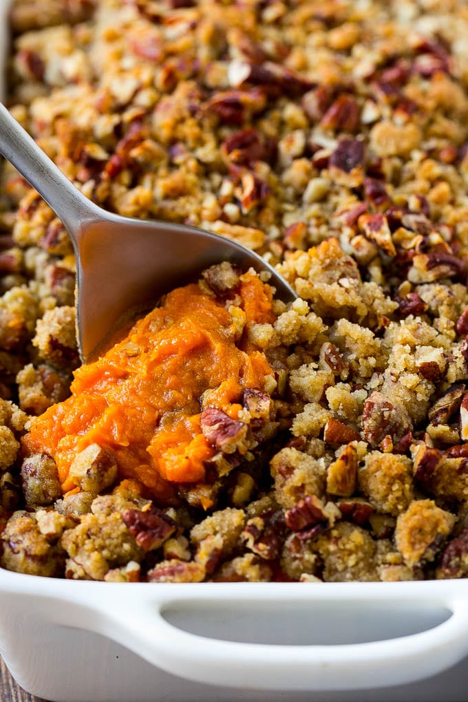 Sweet Potato Casserole with Pecans Recipe | Sweet Potato Casserole | Sweet Potato Side Dish #sweetpotatoes #thanksgiving #pecans #casserole #sidedish #holiday #fall #uzhal A dish of sweet potato casserole with pecans with a serving spoon in it.