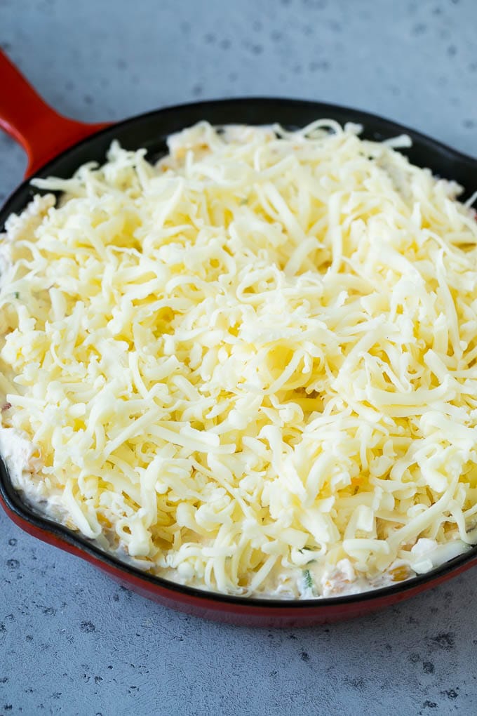 Corn Dip Recipe | Hot Cheese Dip | Bacon Dip #corn #dip #bacon #cheese #appetizer #snack #uzhal A skillet of corn dip covered with shredded cheese.