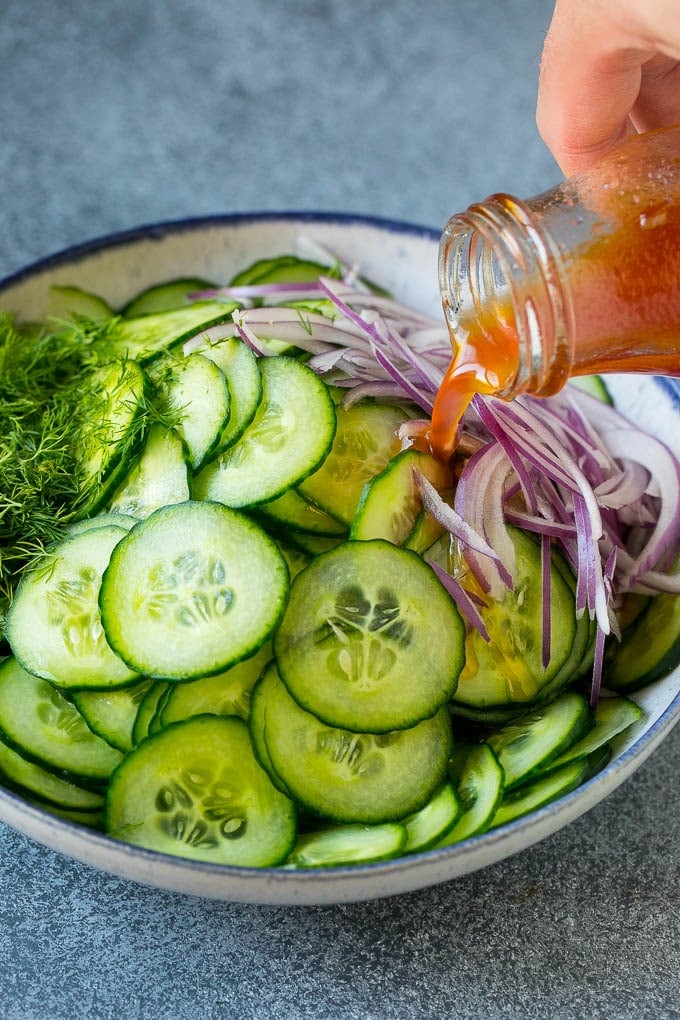 Dressing being poured over sliced vegetables and fresh dill.