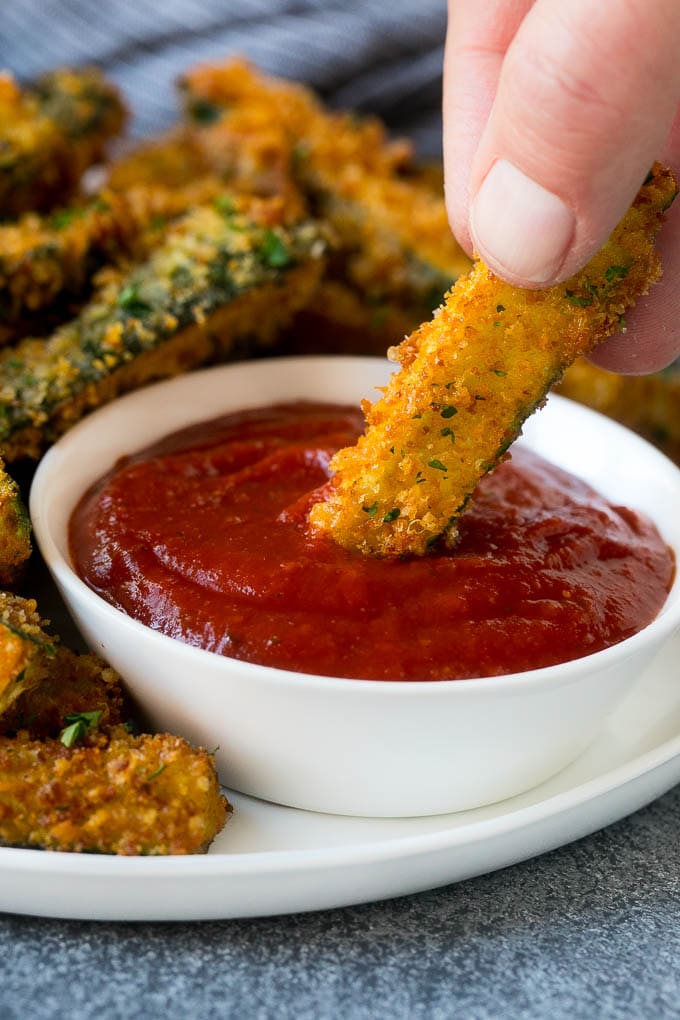 Fried Zucchini Recipe | Zucchini Fries | Zucchini Recipe #appetizer #zucchini #snack #uzhal A hand dipping a piece of fried zucchini into marinara sauce.