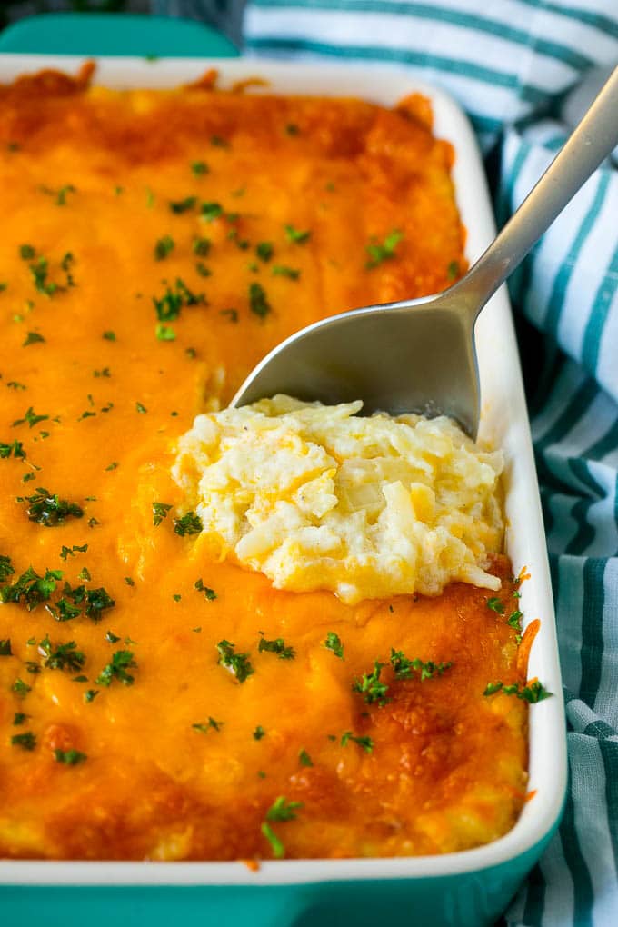 Hash Brown Casserole | Potato Casserole | Hash Brown Side Dish #potatoes #cheese #casserole #sidedish #uzhal Hash brown casserole with potatoes, cheddar cheese, onions and sour cream, with a serving spoon in the dish.