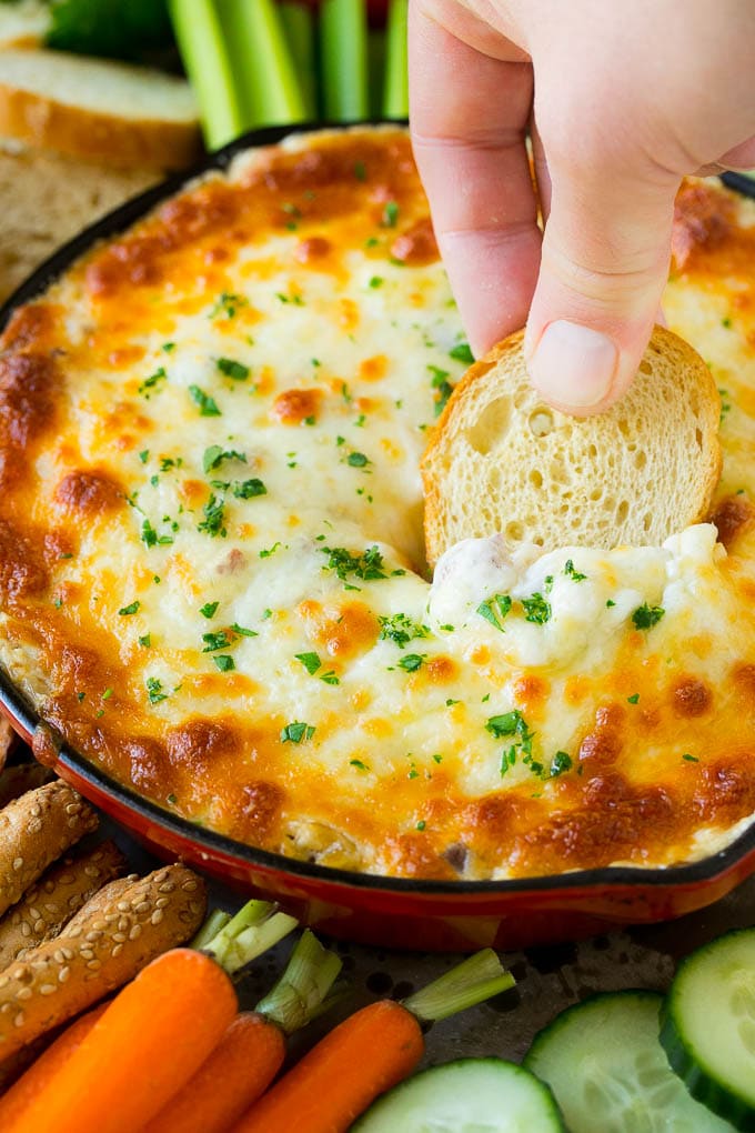 Reuben Dip Recipe | Corned Beef Dip | Cheese Dip #dip #cheese #cornedbeef #appetizer #lowcarb #keto #uzhal A hand scooping out a serving of Reuben dip with baguette.
