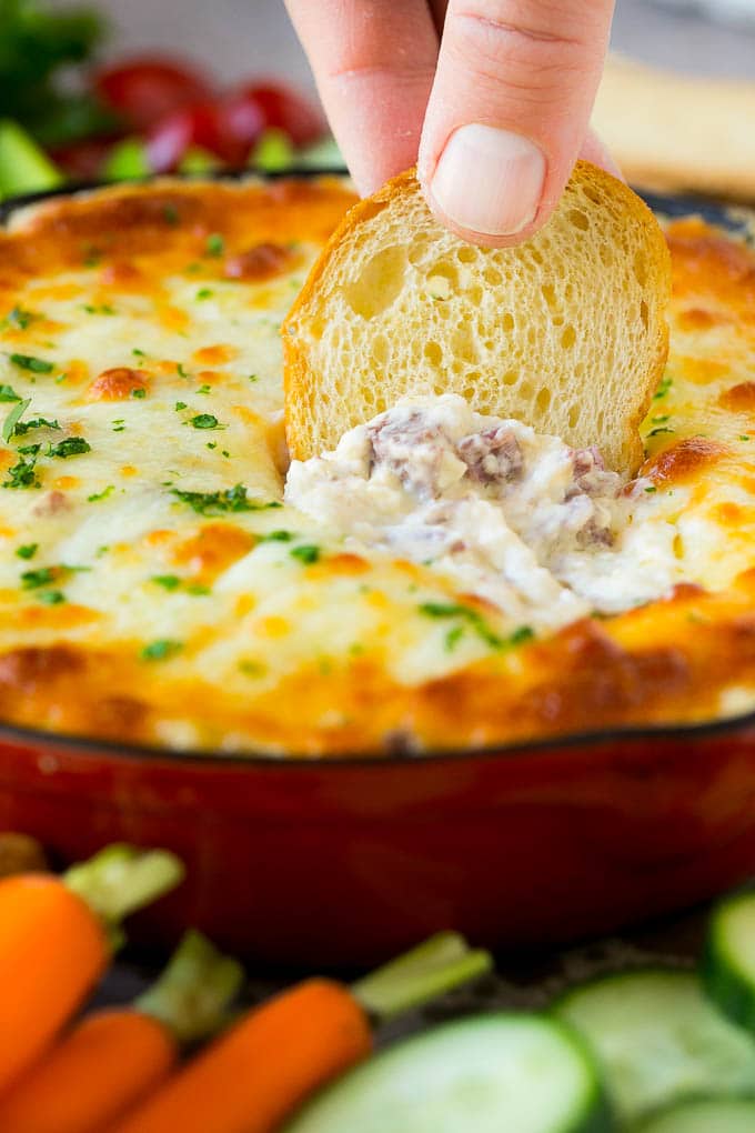 Reuben Dip Recipe | Corned Beef Dip | Cheese Dip #dip #cheese #cornedbeef #appetizer #lowcarb #keto #uzhal A baguette chip dipping into a skillet of Reuben dip.