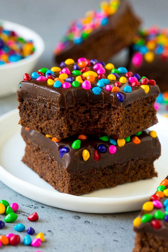 Cosmic Brownies Recipe | Cocoa Brownies | Frosted Brownies #brownies #chocolate #dessert #uzhal #sprinkles A stack of cosmic brownies on a plate with a bite taken out of one.