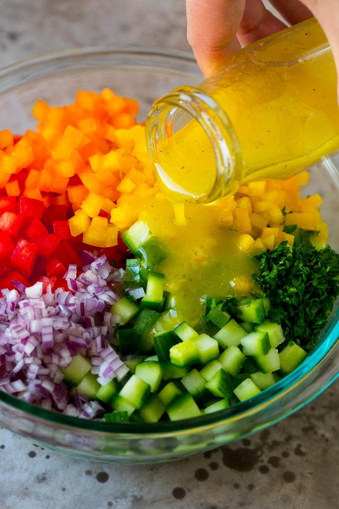 Israeli Salad Recipe | Cucumber Salad | Tomato Salad | Chopped Salad #salad #cleaneating #healthy #glutenfree #lowcarb #keto #sidedish #lunch #uzhal Lemon dressing being poured over chopped vegetables.