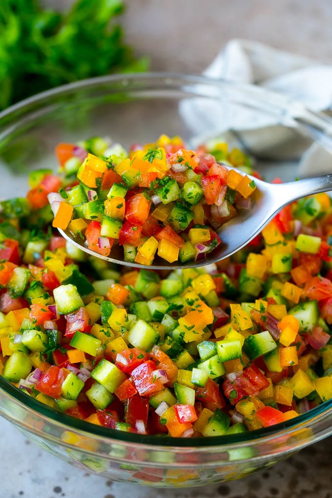 Israeli Salad Recipe | Cucumber Salad | Tomato Salad | Chopped Salad #salad #cleaneating #healthy #glutenfree #lowcarb #keto #sidedish #lunch #uzhal A spoon holding up a serving of Israeli salad.