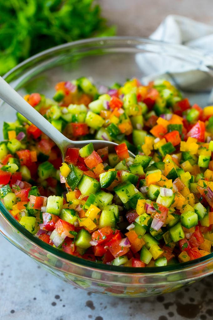 Israeli Salad Recipe | Cucumber Salad | Tomato Salad | Chopped Salad #salad #cleaneating #healthy #glutenfree #lowcarb #keto #sidedish #lunch #uzhal A bowl of Israeli salad with a serving spoon in it.