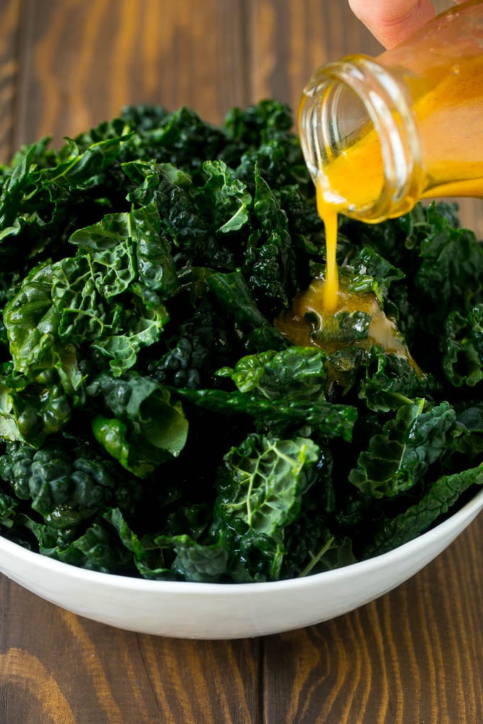 Apple Kale Salad Recipe | Kale Recipe | Fall Salad #kale #apples #bacon #salad #feta #dinner #lunch #uzhal Dressing being poured over dinosaur kale leaves.