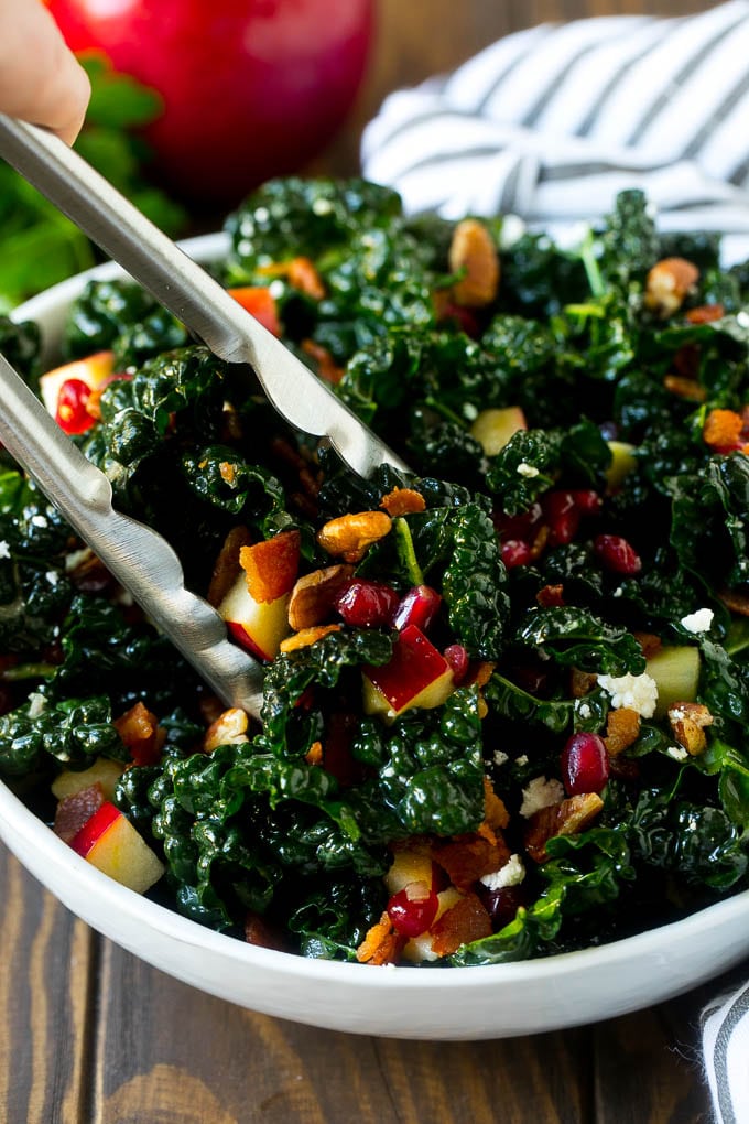 Apple Kale Salad Recipe | Kale Recipe | Fall Salad #kale #apples #bacon #salad #feta #dinner #lunch #uzhal Tongs in a bowl of kale and apple salad.
