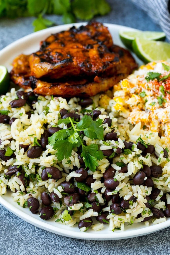 Black Beans and Rice Recipe | Cuban Black Beans | Beans and Rice #beans #rice #blackbeans #sidedish #glutenfree #dinner #uzhal A plate of black beans and rice with grilled pork and Mexican corn.