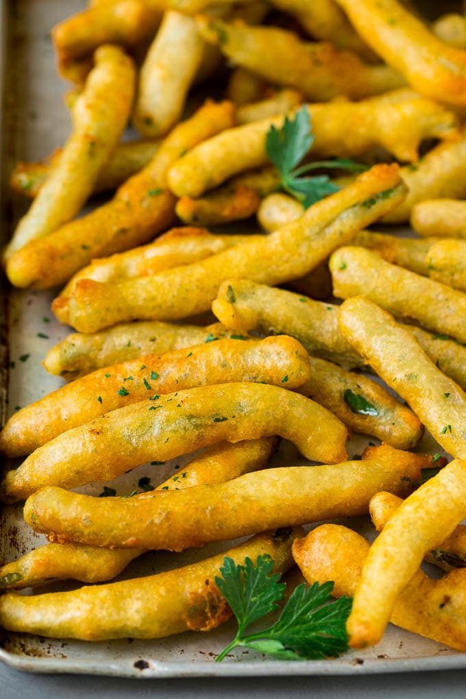 Fried Green Beans Recipe | Green Beans #greenbeans #appetizer #snack #uzhal A sheet pan of fried green beans garnished with chopped parsley.