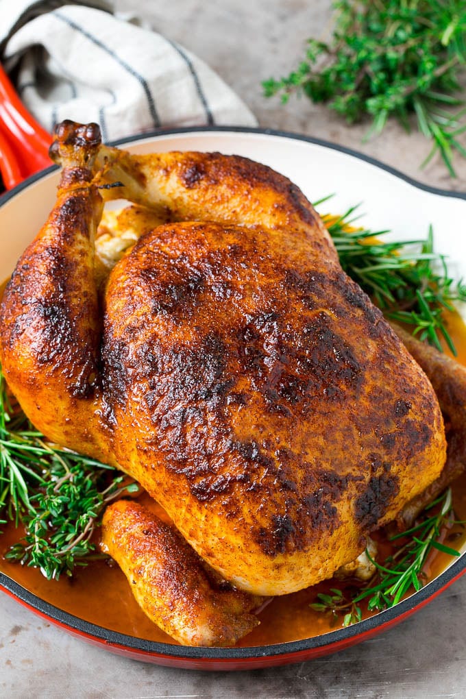 Rotisserie Chicken Recipe | Roasted Chicken #chicken #dinner #uzhal #comfortfood A rotisserie chicken in a red skillet with sprigs of fresh herbs.