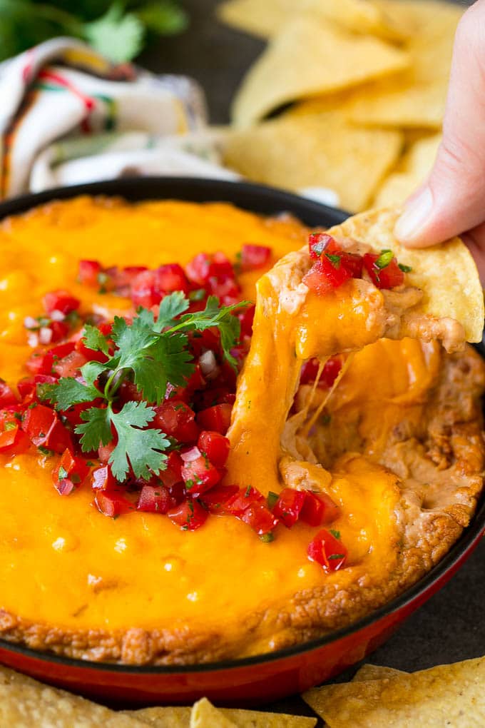 Bean Dip Recipe | Mexican Dip #dip #appetizer #mexicanfood #beans #cheese #uzhal A tortilla chip scooping out a serving of Mexican bean dip.