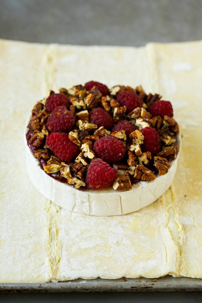 Baked Brie Recipe | Pastry Wrapped Brie #brie #cheese #appetizer #pecans #raspberries #uzhal A wheel of cheese topped with jam, raspberries and pecans.
