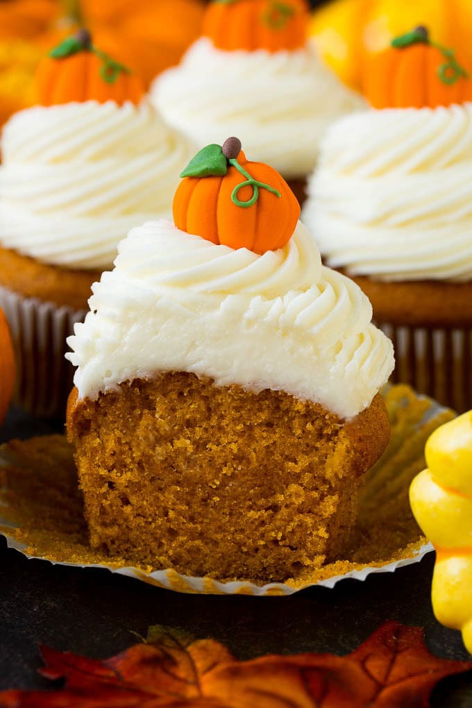Pumpkin Cupcakes Recipe | Pumpkin Cake #cake #cupcakes #pumpkin #frosting #baking #fall #thanksgiving #uzhal A pumpkin cupcake cut in half, surrounded by fall decorations.