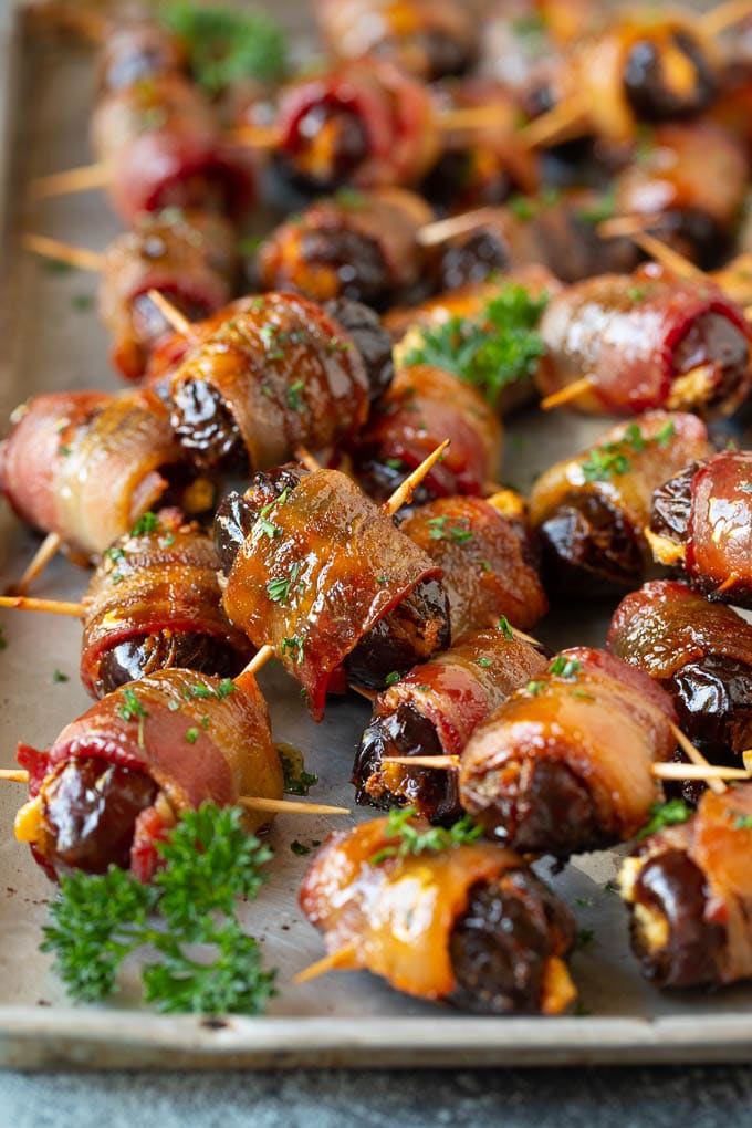 Bacon Wrapped Dates #appetizer #bacon #dates #cheese #uzhal Bacon wrapped dates on a sheet pan garnished with parsley.