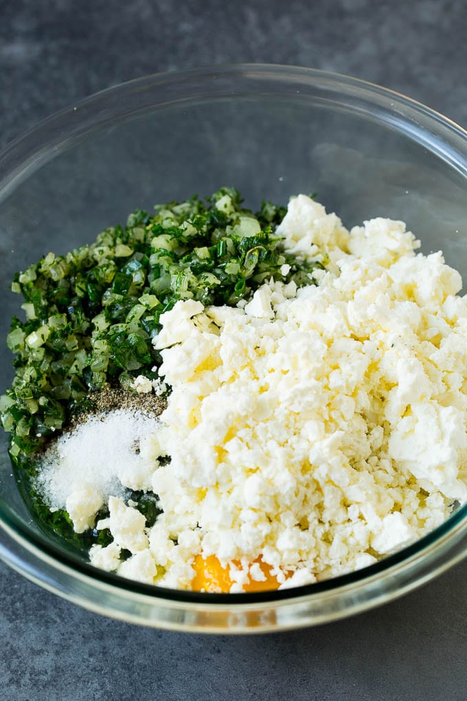 Spanakopita Recipe #appetizer #snack #spinach #cheese #uzhal Spinach, onions, herbs and feta cheese in a bowl.