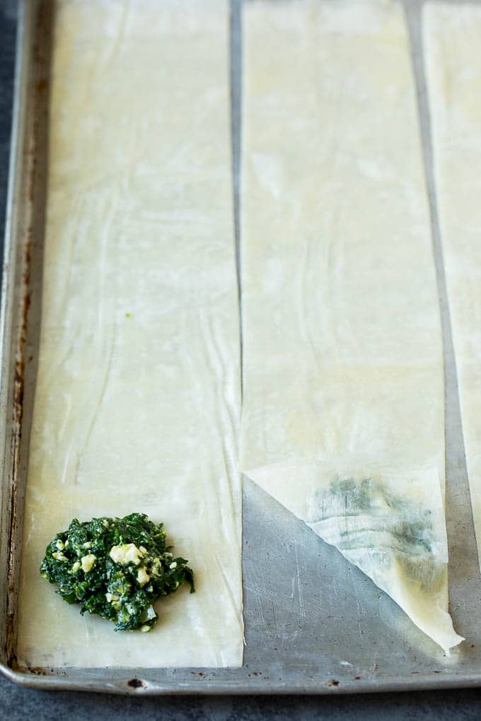 Spanakopita Recipe #appetizer #snack #spinach #cheese #uzhal Strips of phyllo dough with spoonfuls of filling on top.