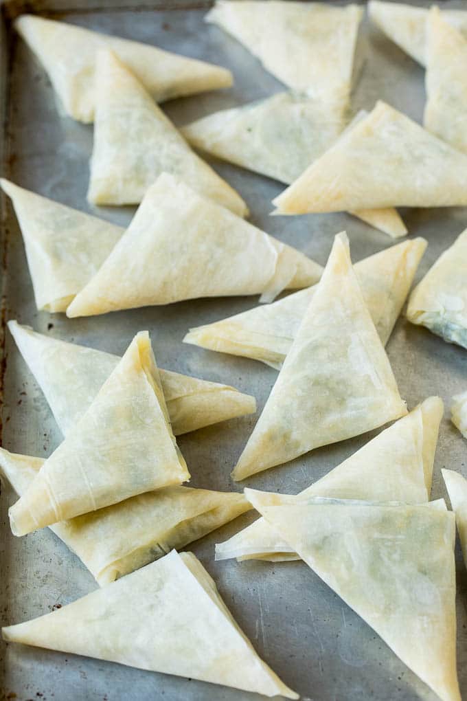 Spanakopita Recipe #appetizer #snack #spinach #cheese #uzhal Folded stuffed phyllo triangles on a sheet pan.