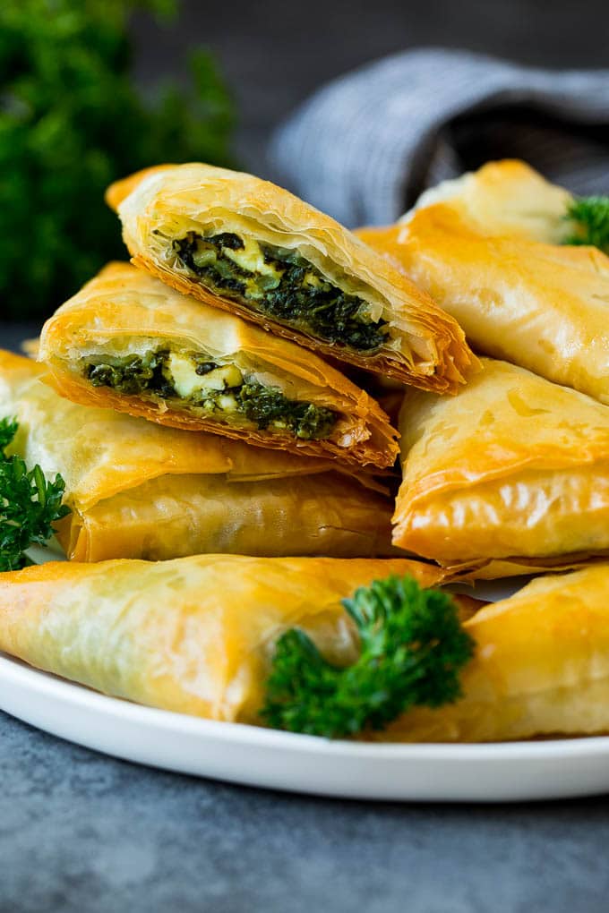 Spanakopita Recipe #appetizer #snack #spinach #cheese #uzhal A plate of spanakopita with two cut in half.