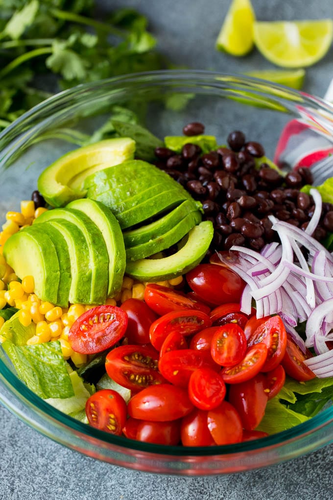 Mexican Salad Recipe #salad #corn #beans #avocado #tomatoes #uzhal Lettuce, tomatoes, onion, corn, avocado and black beans in a bowl.