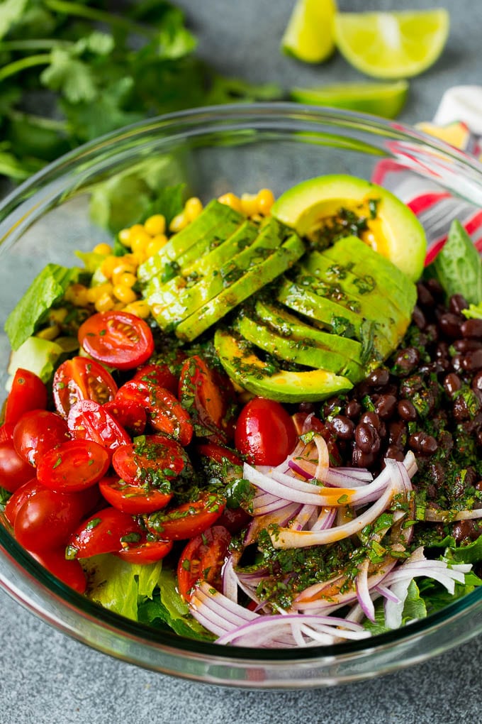 Mexican Salad Recipe #salad #corn #beans #avocado #tomatoes #uzhal Dressing poured over a bowl of lettuce, tomatoes, avocado and beans.