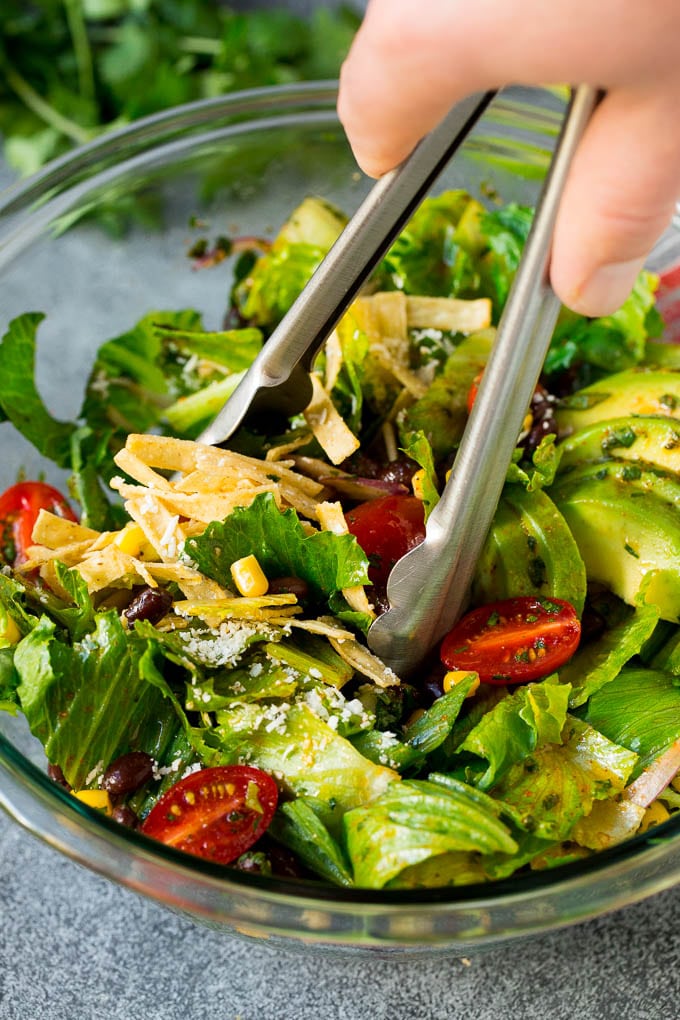 Mexican Salad Recipe #salad #corn #beans #avocado #tomatoes #uzhal Tongs serving up a portion of Mexican salad.