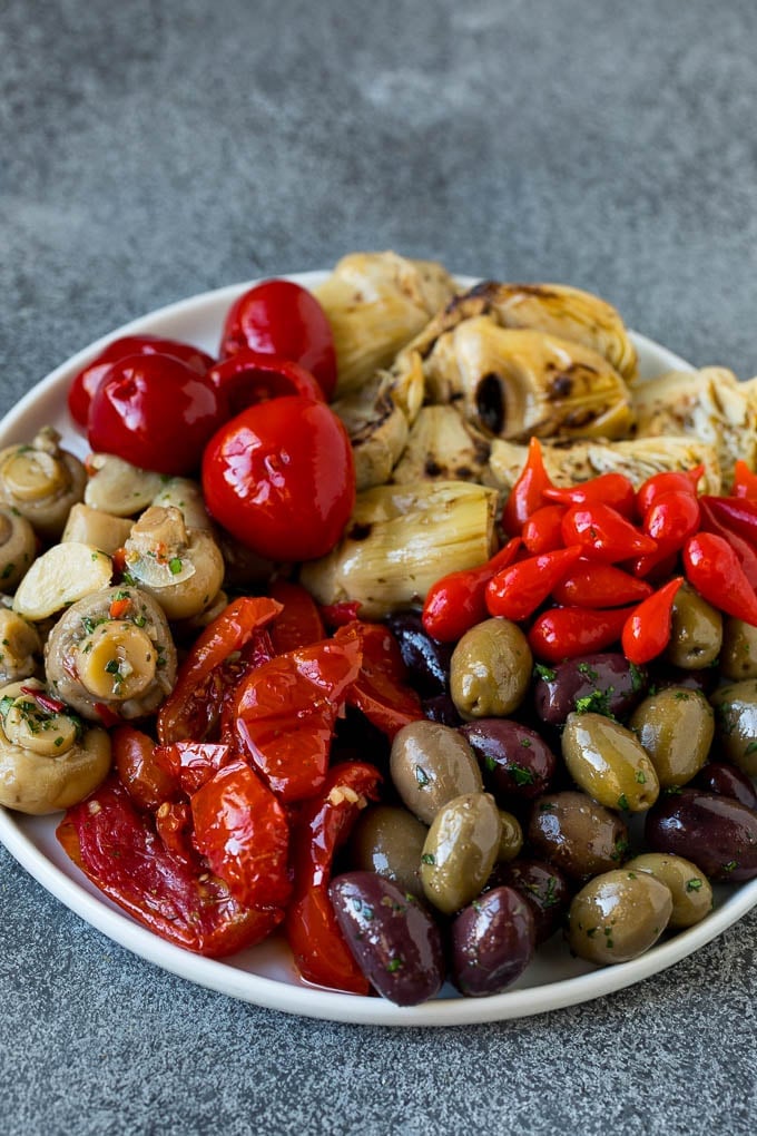 This mezze platter is filled with Mediterranean delicacies including dolmas, hummus, vegetables, pita bread and salads. #appetizer #uzhal A plate of olives, peppers and grilled artichokes.