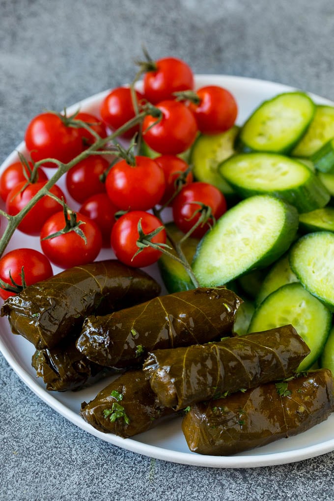 This mezze platter is filled with Mediterranean delicacies including dolmas, hummus, vegetables, pita bread and salads. #appetizer #uzhal A plate of cherry tomatoes, cucumber slices and dolmas.