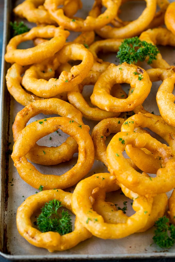 Crispy homemade onion rings that are fried in a flavorful beer batter. #onions #uzhal #appetizer Beer battered onion rings on a sheet pan.